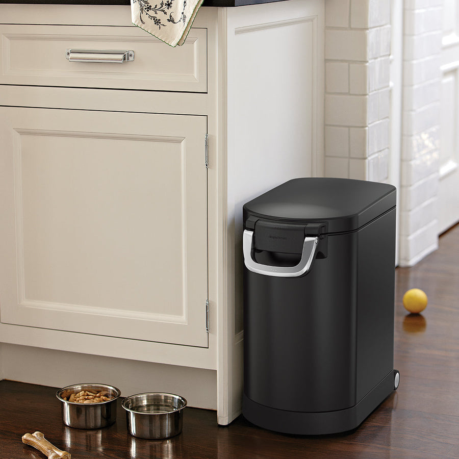 Lifestyle view of Simplehuman Medium Pet Food Can, Matte Black, stored neatly by kitchen cabinets, airtight seal.