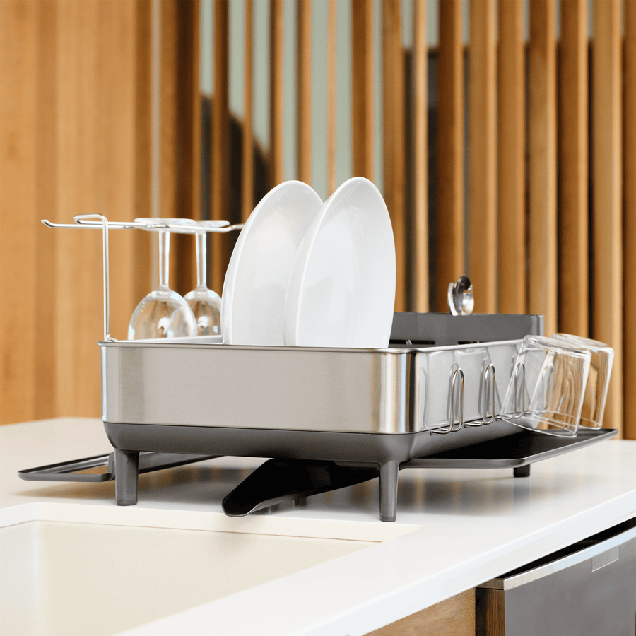Simplehuman Brushed Stainless Steel Steel Frame Dishrack angled view on a countertop, drying plates and wine glasses with integrated drainage.