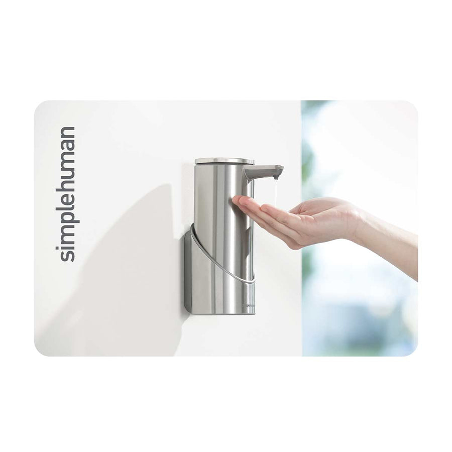 Simplehuman Wall Mount Sensor Pump in Brushed Stainless Steel dispensing soap onto a hand, touch-free operation, space-saving design.
